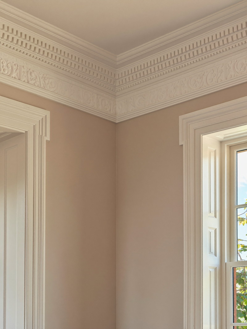 Newly installed crown molding in a classic colonial dining room: crisp white detailed profile meeting a soft warm wall, perfect mitered corner, warm light from
