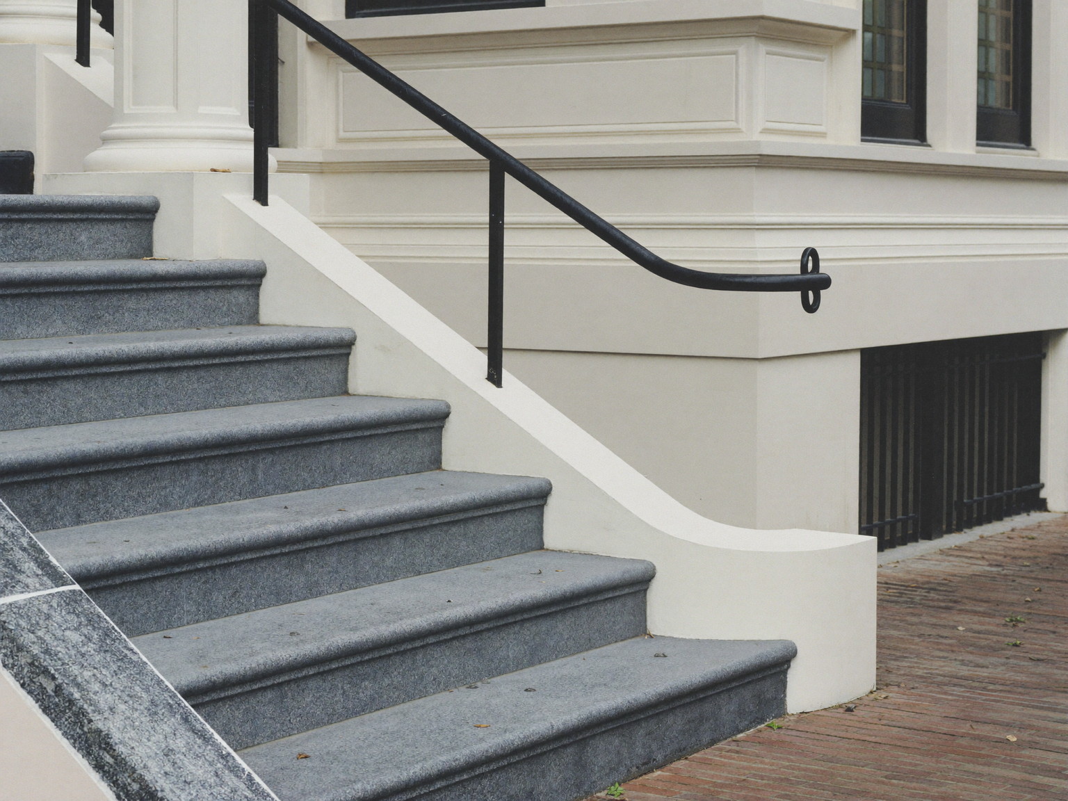 Repaired front entry steps of a classic Wellesley colonial: bluestone treads, crisp white risers, a simple repainted black iron handrail, brick walk below