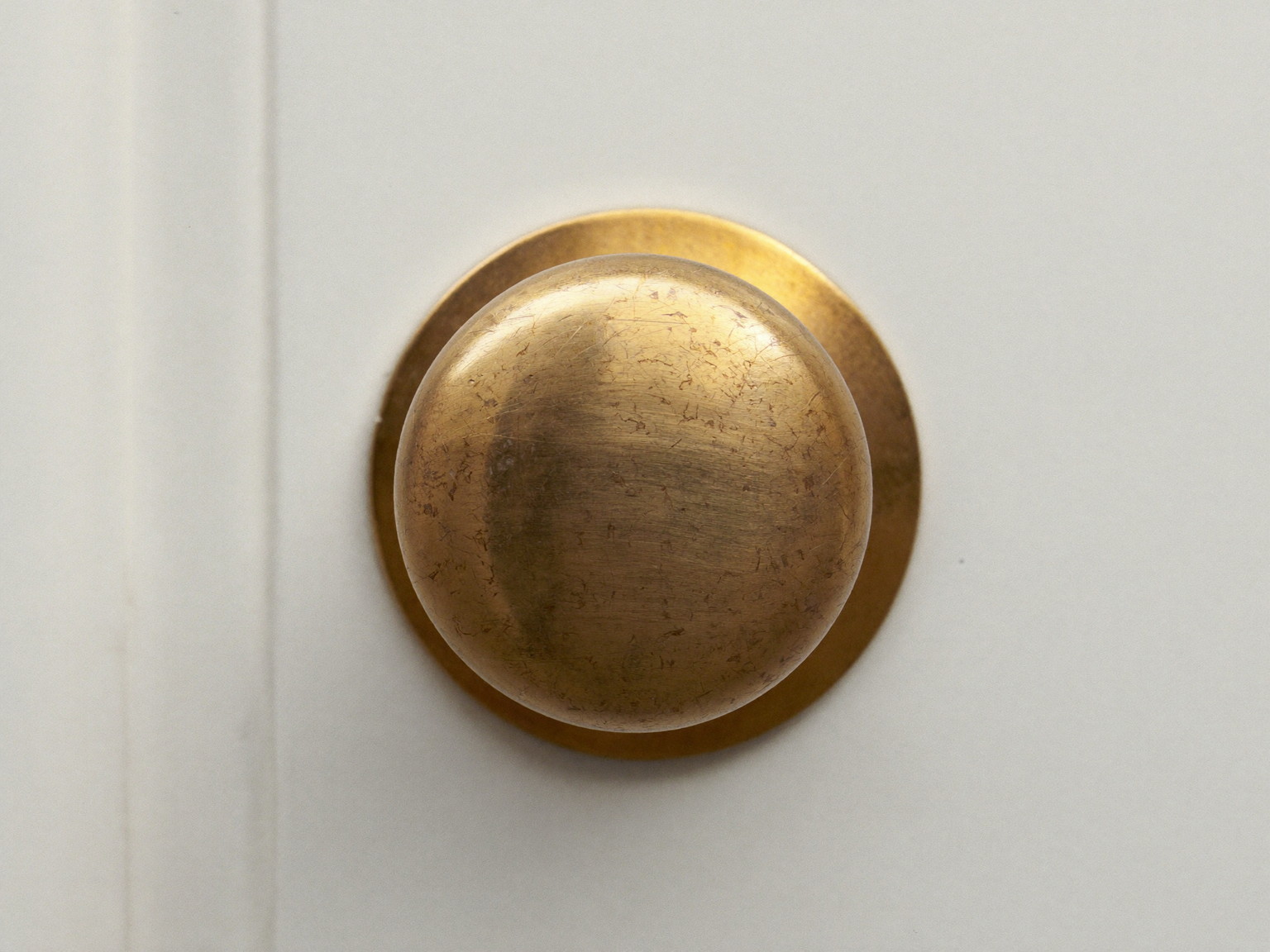 Macro photograph of an aged solid brass door knob with a perfectly plain smooth polished dome face and matching plain rosette on a white paneled colonial door