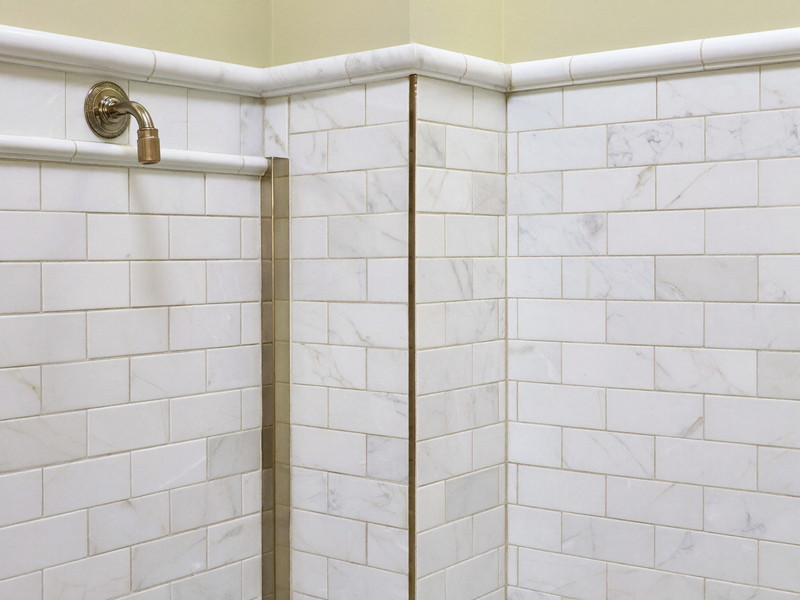 Freshly regrouted white marble subway tile in a colonial bathroom corner: clean bright grout lines, every tile flat and straight, polished nickel fitting at