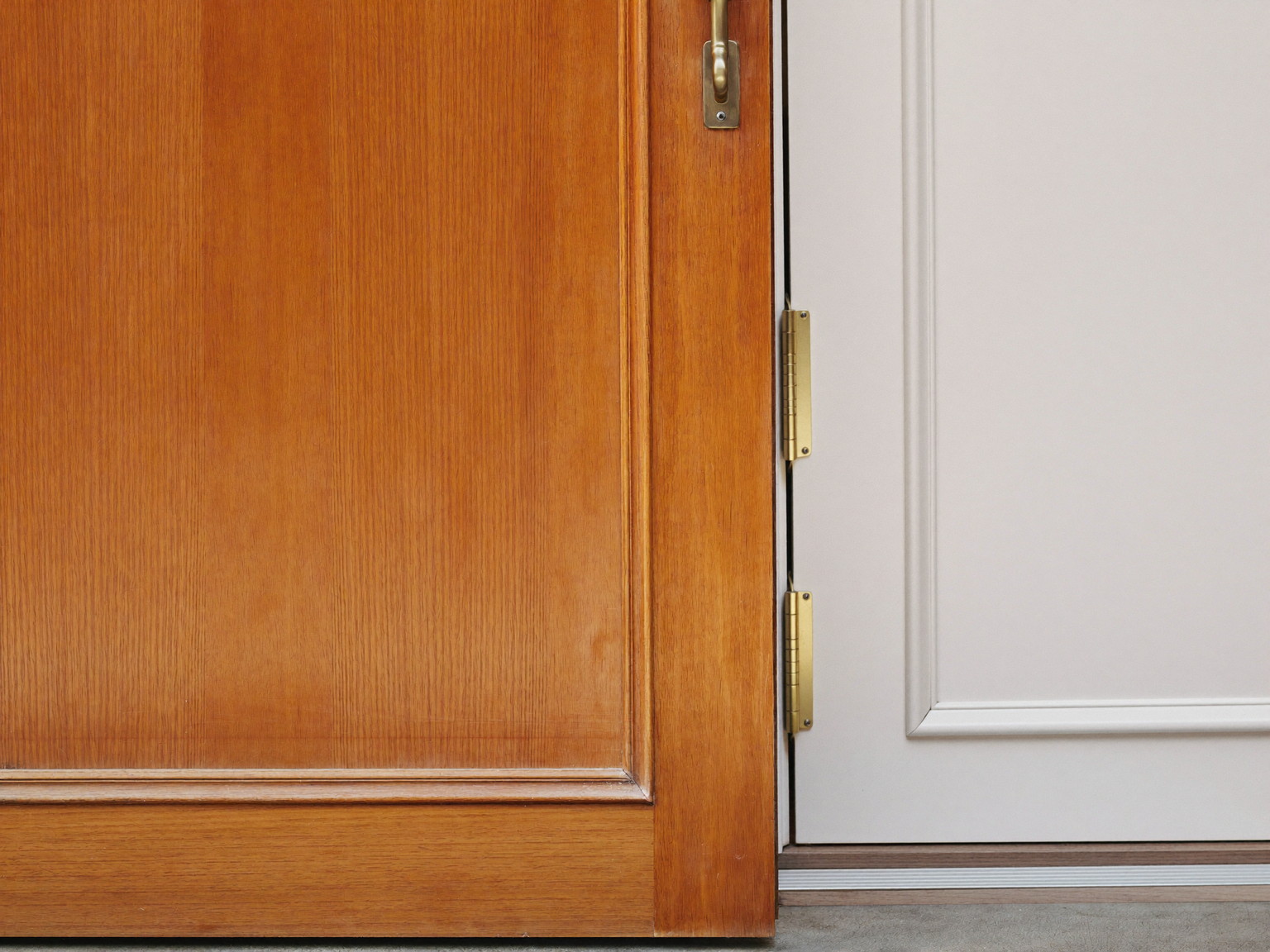 A classic wooden front door standing ajar in its freshly serviced frame seen from the side: smooth refreshed painted edge and one clean brass hinge visible
