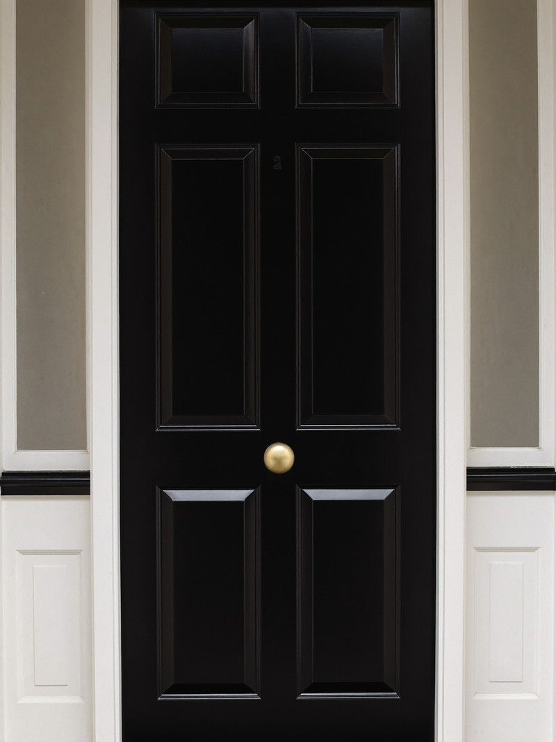 A freshly painted glossy black front door on a classic Wellesley colonial: smooth deep finish, white paneled surround with sidelights of clear glass, smooth