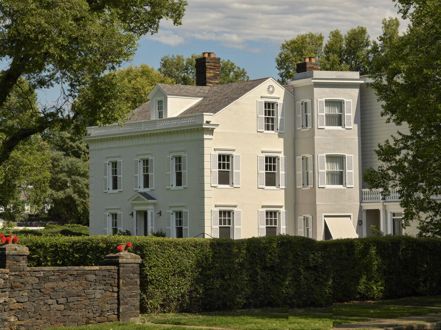 A leafy Wellesley Massachusetts street of classic freshly painted homes: white and soft gray colonials and capes with black shutters and bright trim, stone