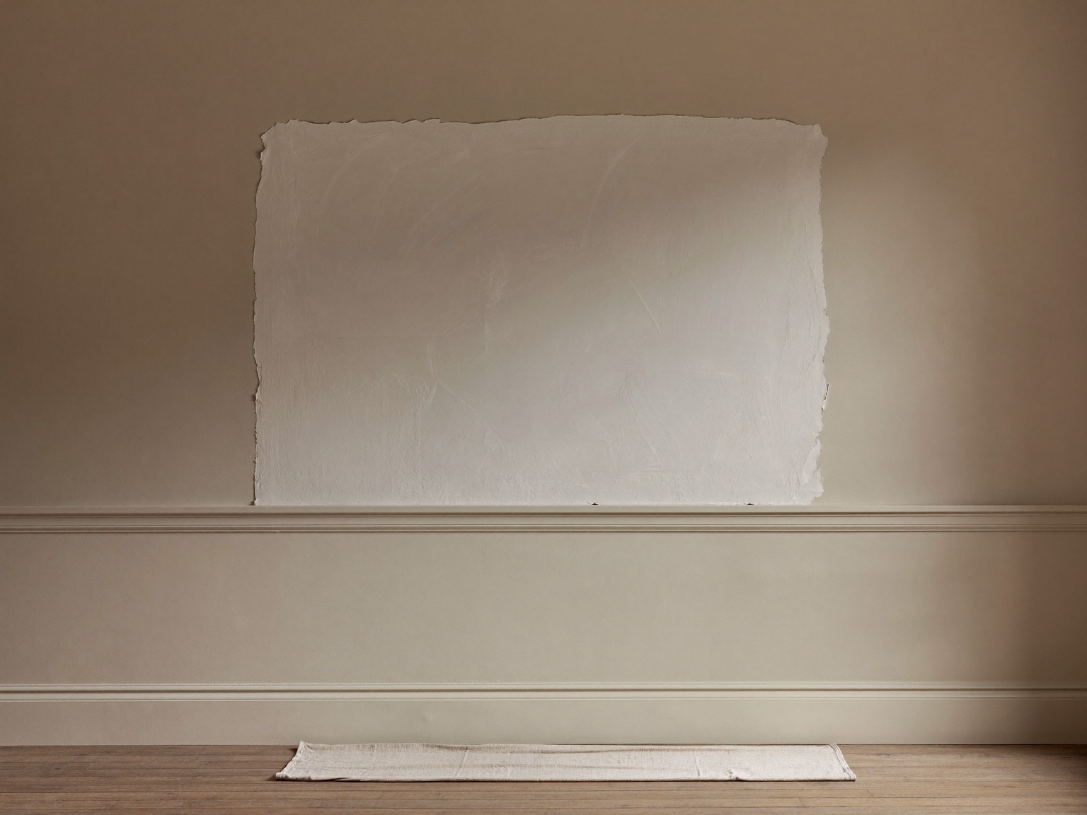 A freshly skim-coated plaster wall section drying in soft raking light in a classic colonial room, smooth flat even finish, tidy canvas drop cloth below